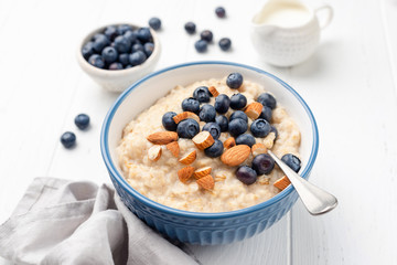 Healthy breakfast oatmeal porridge in bowl with blueberries and almonds on white wooden table...