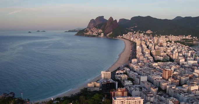 Flying along Ipanema Beach overlooking beautiful morning light on buildings by the ocean. Wide angle panorama of Rio de Janeiro, Brazil and Mountains on the horizon