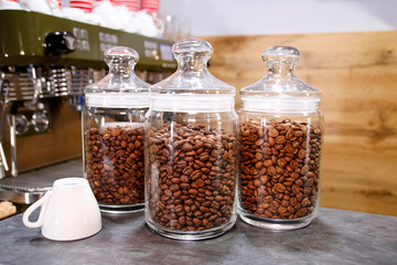 Glass bank with coffee grains costs on a table on a wood background