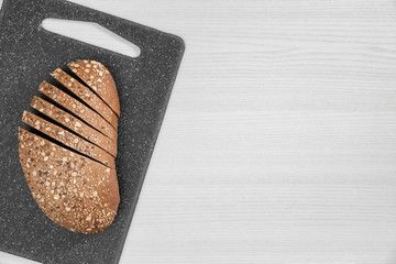Sliced bread with seeds and flakes on grey board on white background.