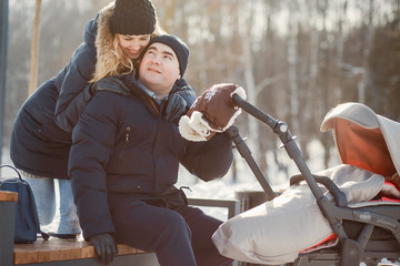 Obraz premium Beautiful family in a winter forest. Mother and father sitting on a bench witn carriage.