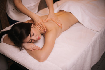 Female masseuse does shoulder and back massage to young woman in spa centre, close-up. Beautiful girl with perfect skin gets relaxing massage. Concept of professional massage. Concept of body care.