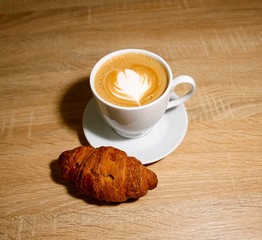 A cup of coffee with heart pattern in a white cup on wooden background