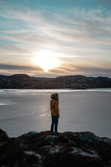 Woman looking at a frozen lake on a beautiful sunny evening in winter Norway.