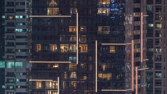 Rows of glowing windows with people in the interior of apartment buildings at night. Modern skyscrapers with glass surface. Concept for business and modern life. Zoom in