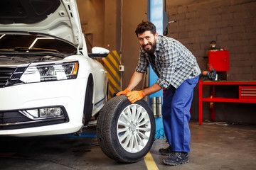full length shot of young auto technician changing tire and looking at the camera in the garage