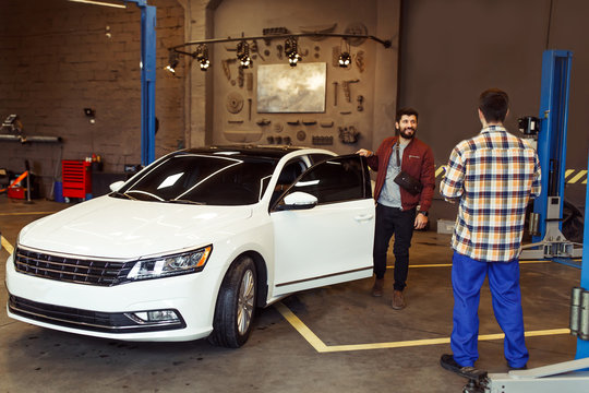 Full Length shot of satisfied male client taking car after repairing and leaving workshop with mechanic