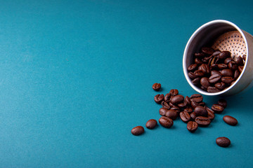 Aluminium filter with brown coffee beans on a teal blue surface with ground beans.