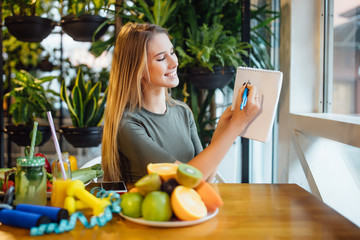 Blonde girl, dietologist working in modern room. Woman writing diet plan on table and using...