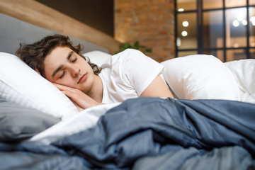 Peacefulness concept. Handsome young man sleeping in bed at modern room