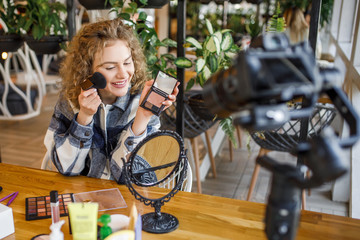Young cute woman showing a makeup palette on camera and recording her video. Woman making a video...
