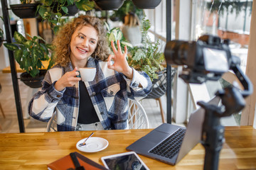 Portrait of smiling woman blogger in casual wear posing to the camera with cup of coffee