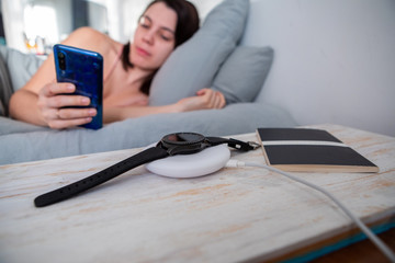 woman surfing internet on cellphone laying in bed smart watch on wireless charger
