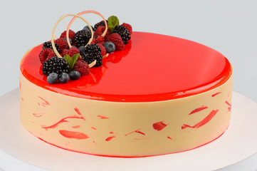 Beautiful festive cake decorated with various berries and red icing on a white dish. White background. Close-up.