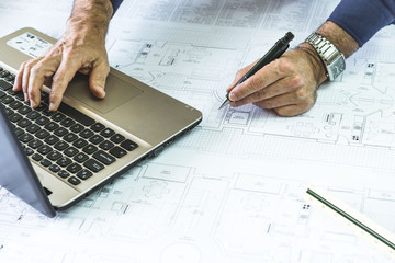 Architect with a mechanical pencil in his hand next to a laptop on blueprints