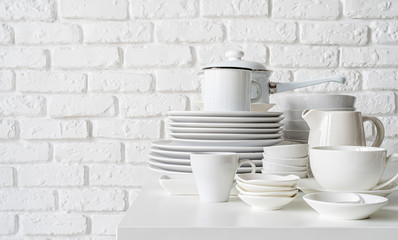 stack of white ceramic dishes and tableware on the table on white brick wall background