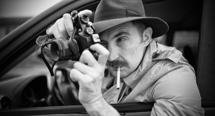 Spy or paparazzo photographer, man using camera in his car, black and white