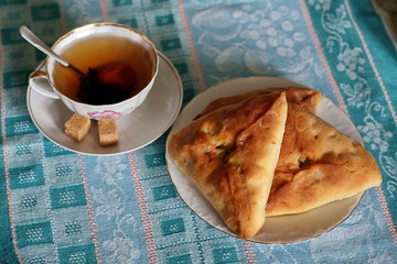 Traditional Tatar dish  echpochmak - a triangle in a plate on a green towel. A cup of traditional Tatar tea with prune and dried apricots.