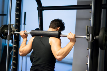 Man doing squats using a squat cage in a gym to train his legs