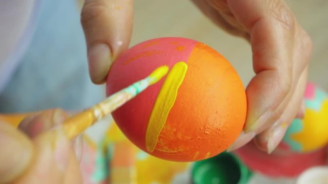Posting: the hand dips the brush into the paint and draws stripes on the Easter egg. Girl draws a striped pattern on an egg. Easter decoration preparing happy easter