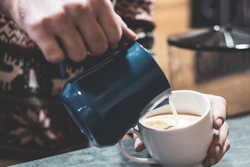 hand of barista making latte or cappuccino coffee pouring milk making latte art