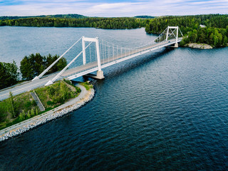 Aerial view of white suspension bridge with car crossing over blue lake in Finland