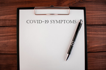 Words COVID-19 symptoms: text written on a shit of paper of notebook on the wooden background. Medical concept.