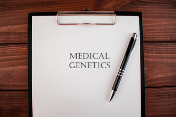 Words medical genetics: text written on a shit of paper of notebook on the wooden background. Medical concept.