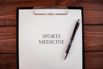 Words sports medicine: text written on a shit of paper of notebook on the wooden background. Medical concept.