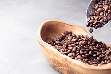 Coffee beans in a wooden bowl made of olive wood and a metal scoop on a light gray background. Space for text.