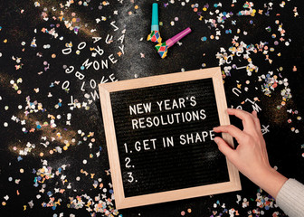 Person setting New Year's Resolutions on a letterboard surrounded by confetti and party blowers
