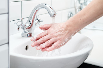 Washing hands with soapy foam, under running water, in the bathroom.