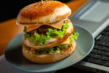 Eating at work place - fast food. burger near laptop. lunch break while you work or sharing online