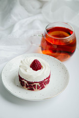 a cake with a white cap of cream and raspberry jelly, next to a transparent mug of amber tea