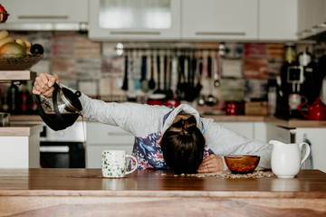 Tired mother, trying to pour coffee in the morning. Woman lying on kitchen table after sleepless night