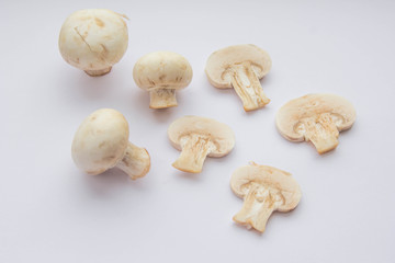 Four raw champignon mushrooms (three whole ones and one cut) at white background