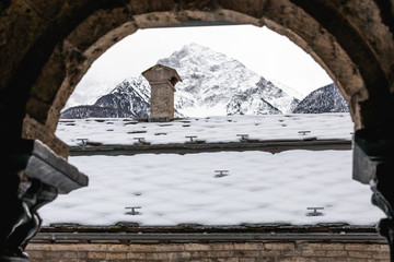 A snow-covered roof with a chimney on the top and distant mountain peaks, as seen from the round...
