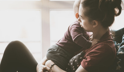 Concerned woman holding and hugging a small child. Mom from the generation of milenials sits by the...