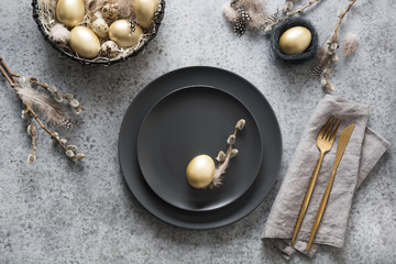 Easter table setting with black and golden eggs on grey table.  Top view.