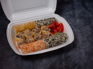Defferent type of rolls or sushi set in a white plastic take-away box on gray stone table.