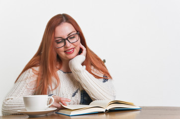 A woman with freckles drinking coffee and reading a book