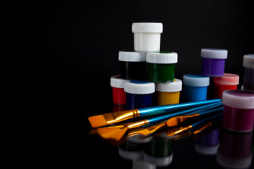 Jars of paint on a black background with a reflection. Paint gouache. Paint brushes.