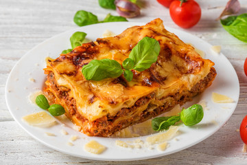 Meat lasagna with fresh basil and parmesan cheese in a plate on white wooden table. close up