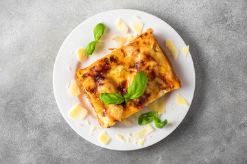 Homemade meat lasagna with fresh basil and parmesan cheese in a plate on gray concrete background. top view