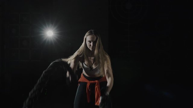 Portrait of a beautiful girl working hard with a rope in a sports gym. Functional training. Motivation. CrossFit Focus Success Concept. Shot on a Red Cinema 4K camera. Professional movie lighting.