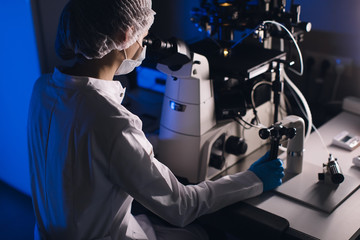 In a Modern Laboratory Scientist Conduct Experiments. Chief Research Scientist Adjusts Specimen in a Petri Dish and Looks on it Into Microscope.