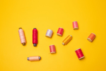 Top view of multi colored thread spools or sewing accessories on a yellow background.