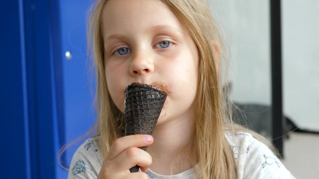 Funny Kid Girl With Fair Hair, Blue Eyes And Dirty Lips Biting Black Chocolate Waffle Icecream Cone. Summertime