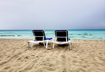 Two loungers, chaise-longues on a cuban beach before storm