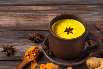 Golden milk or turmeric latte made with curcuma, star anise, ginger and cinnamon on rustic wooden...
